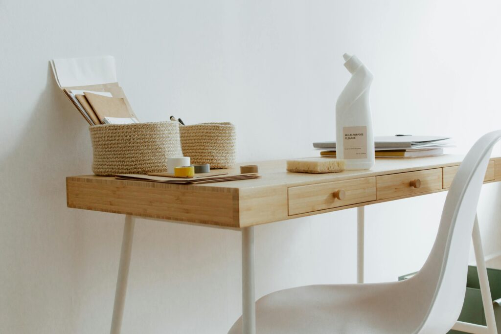 A clean and organized home office desk with cleaning products, papers, and storage baskets.