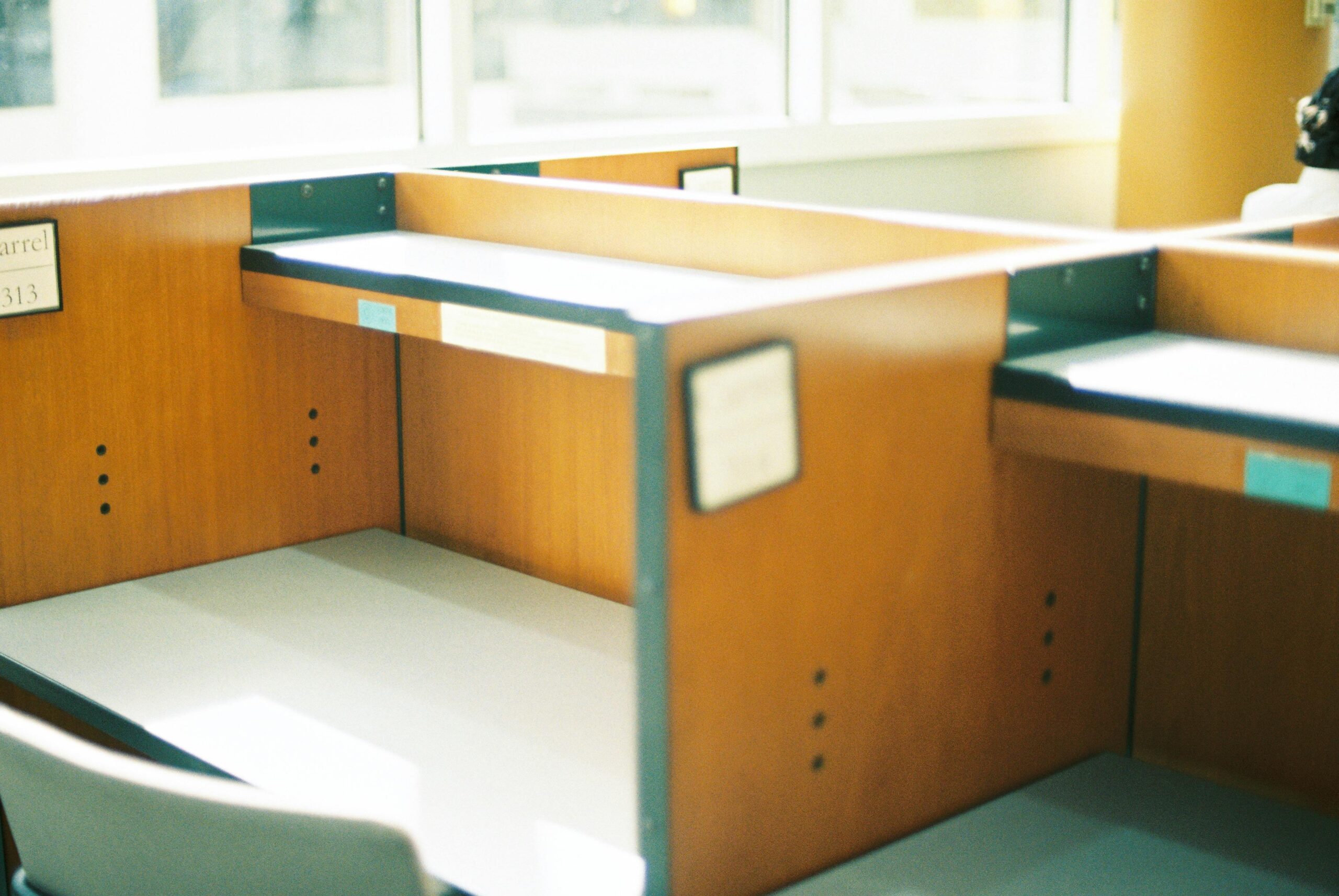 Empty wooden cubicles in a sunlit office space, offering a modern professional ambience.