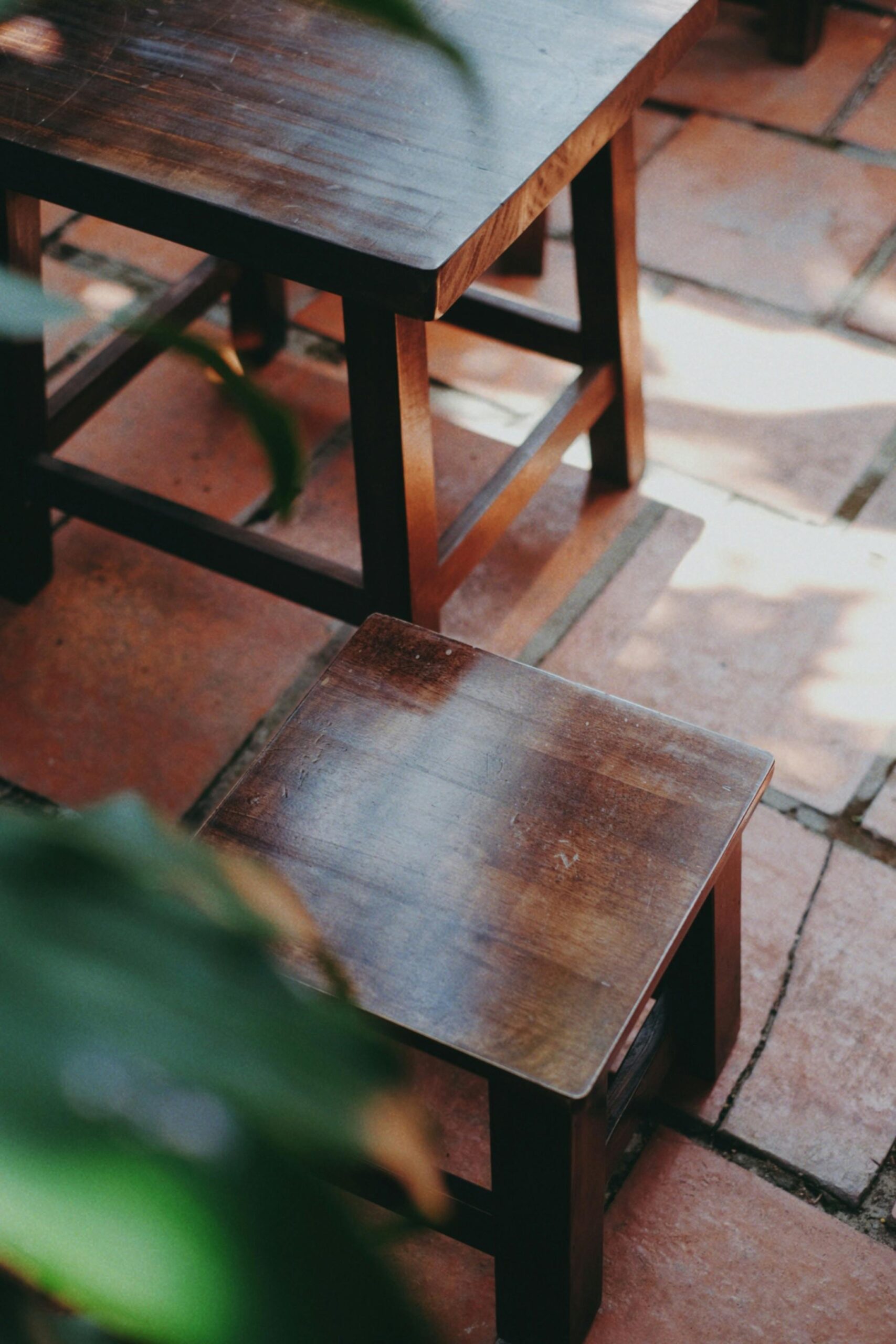 Sunlit patio with rustic wooden tables and stools on terracotta tiles.